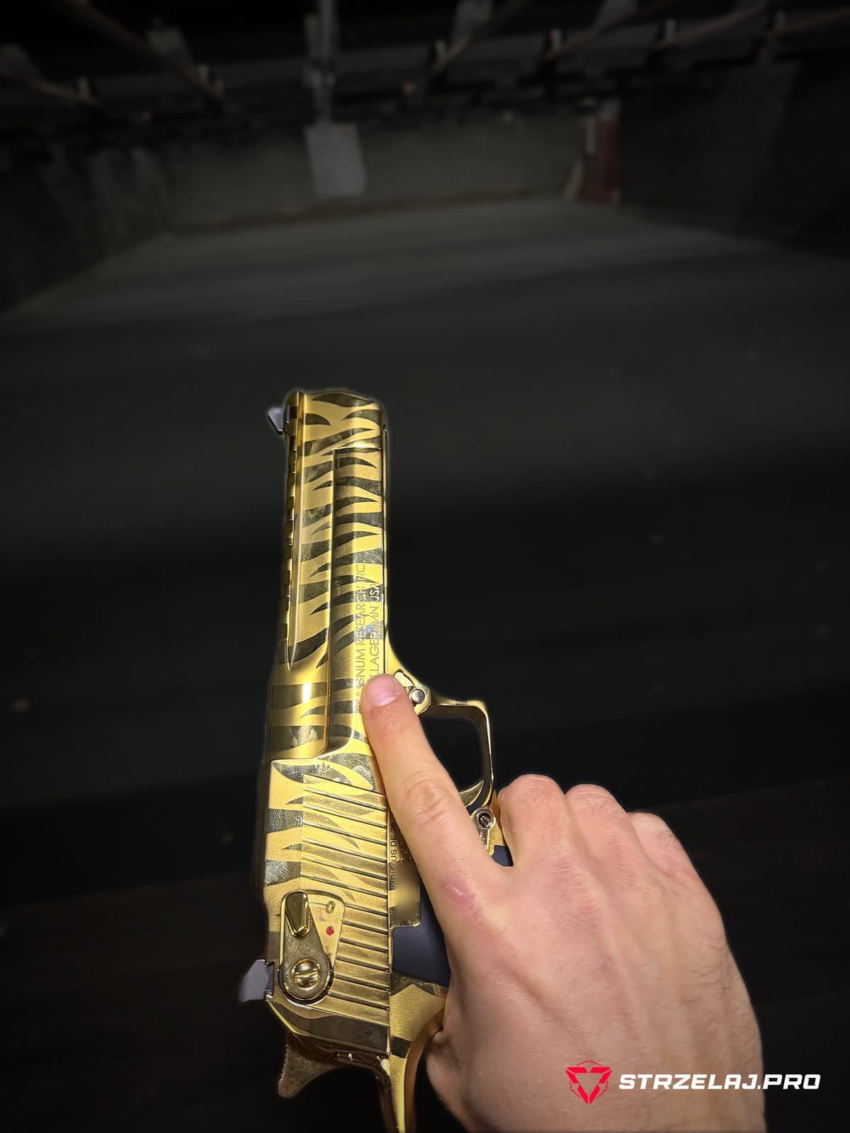 Desert Eagle Mark XIX trzymany na stanowisku strzelnicy krytej, w tle tor i tarcza